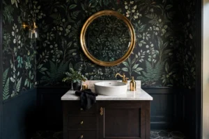 Powder room with bold dark botanical wallpaper and brass mirror