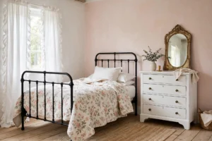 Cozy cottage bedroom with black iron bed, floral quilt, ruffled curtains and pastel walls in soft daylight