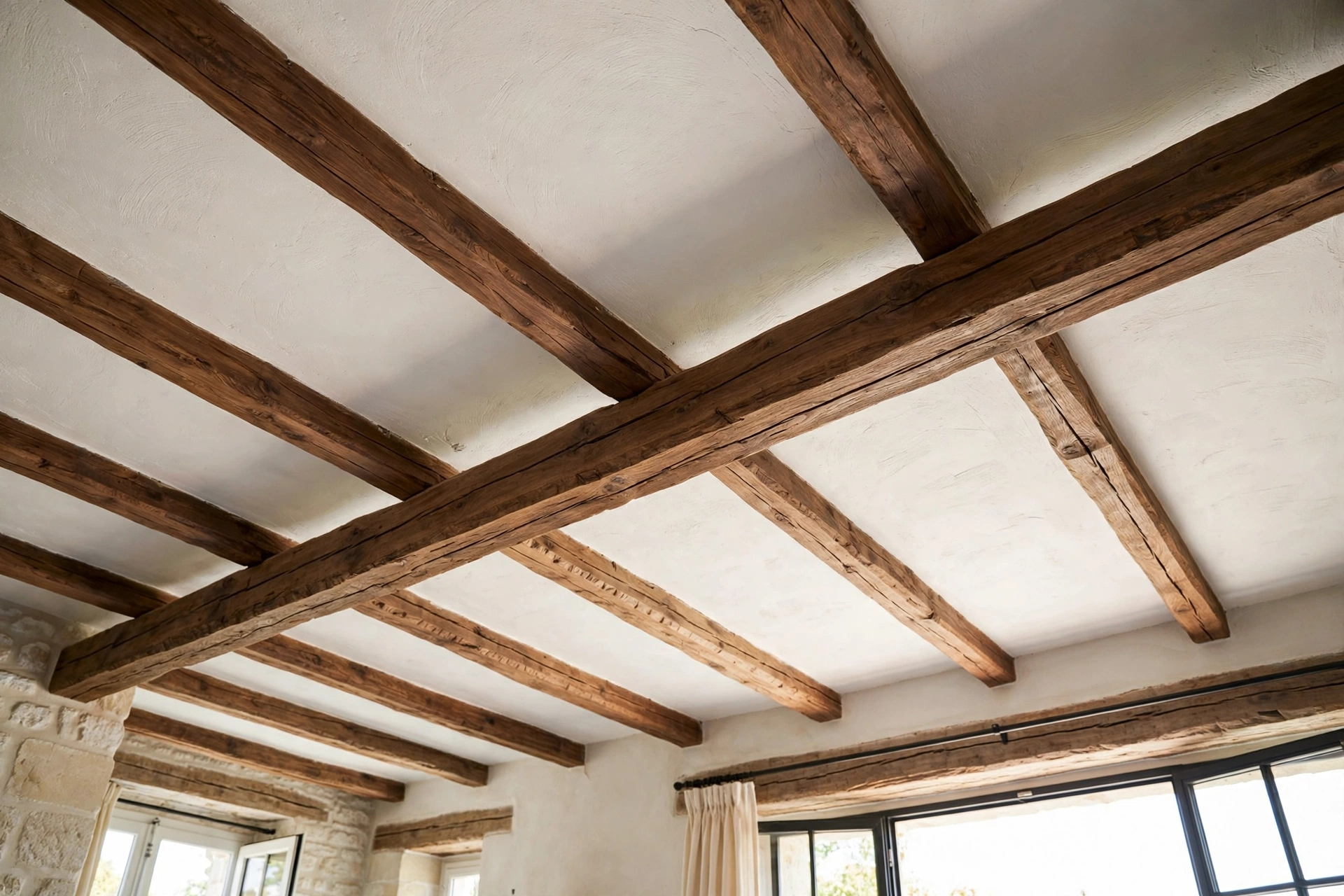 French country living room with rustic walnut wood beams across a plaster ceiling above a farmhouse interior.