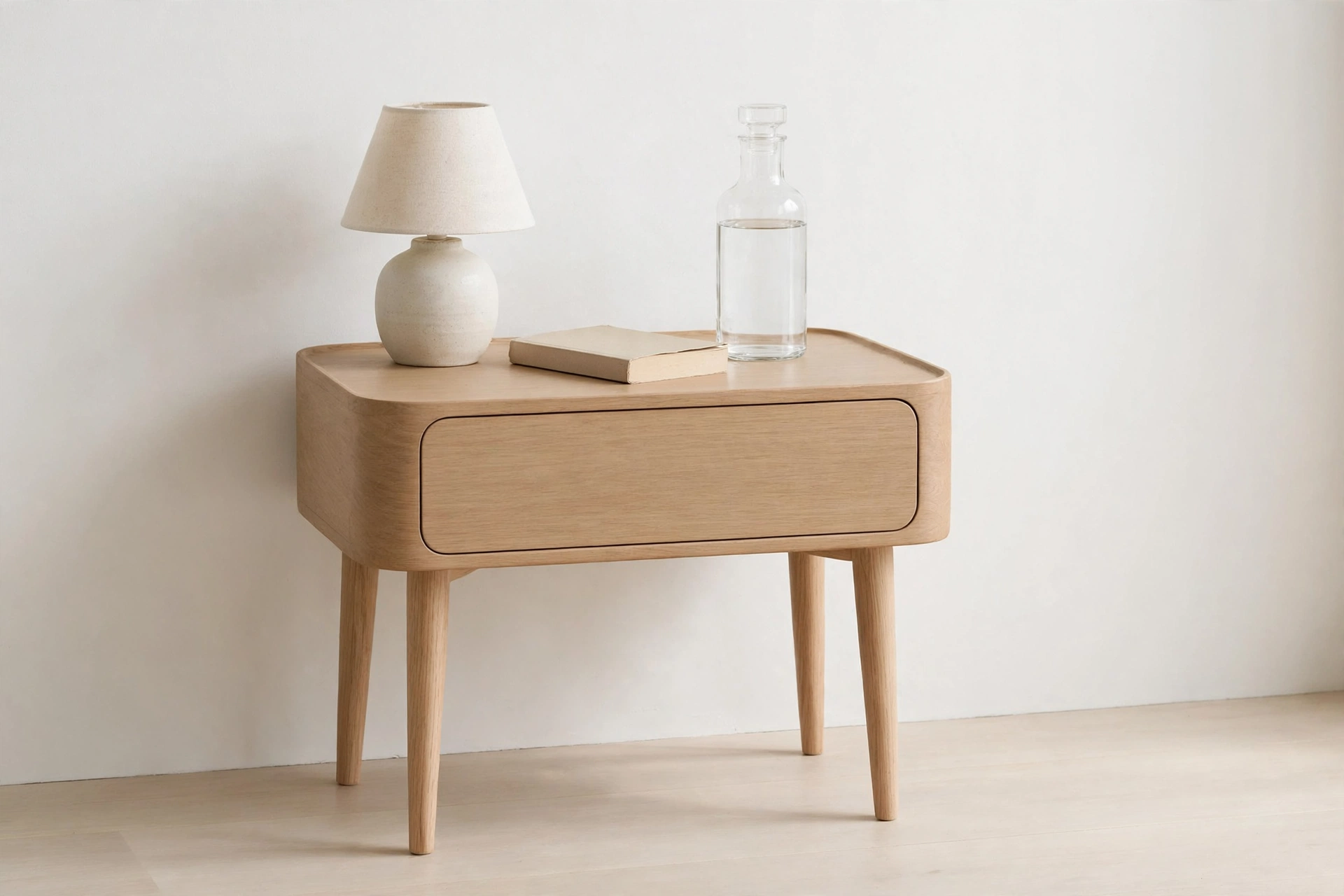 Round-edged light-oak nightstand with ceramic lamp, book and glass carafe