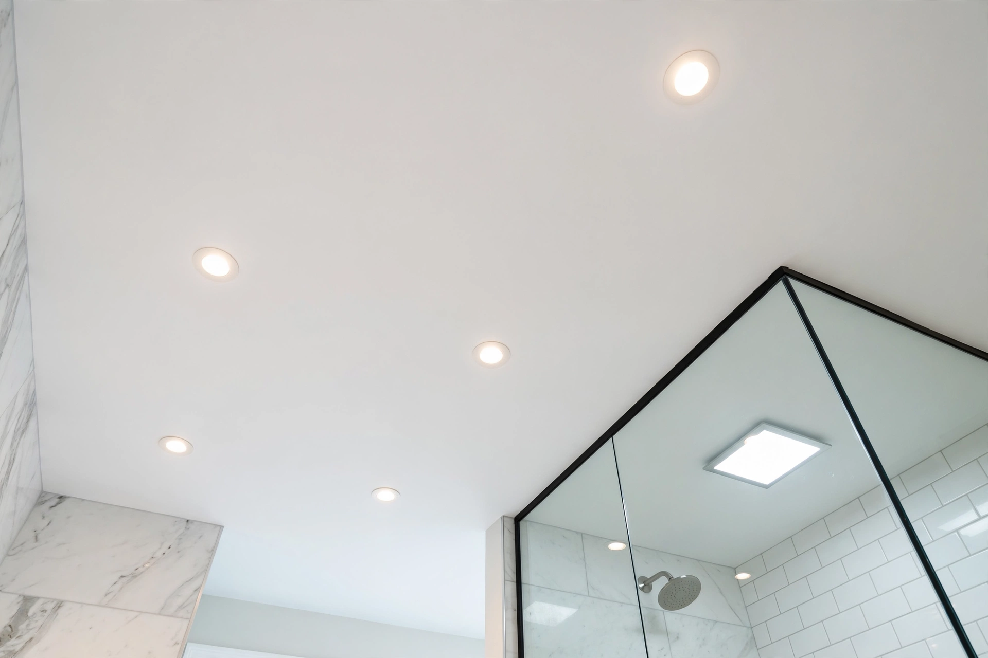 Recessed ceiling lights providing even ambient light in a clean modern bathroom with a damp-rated shower light.