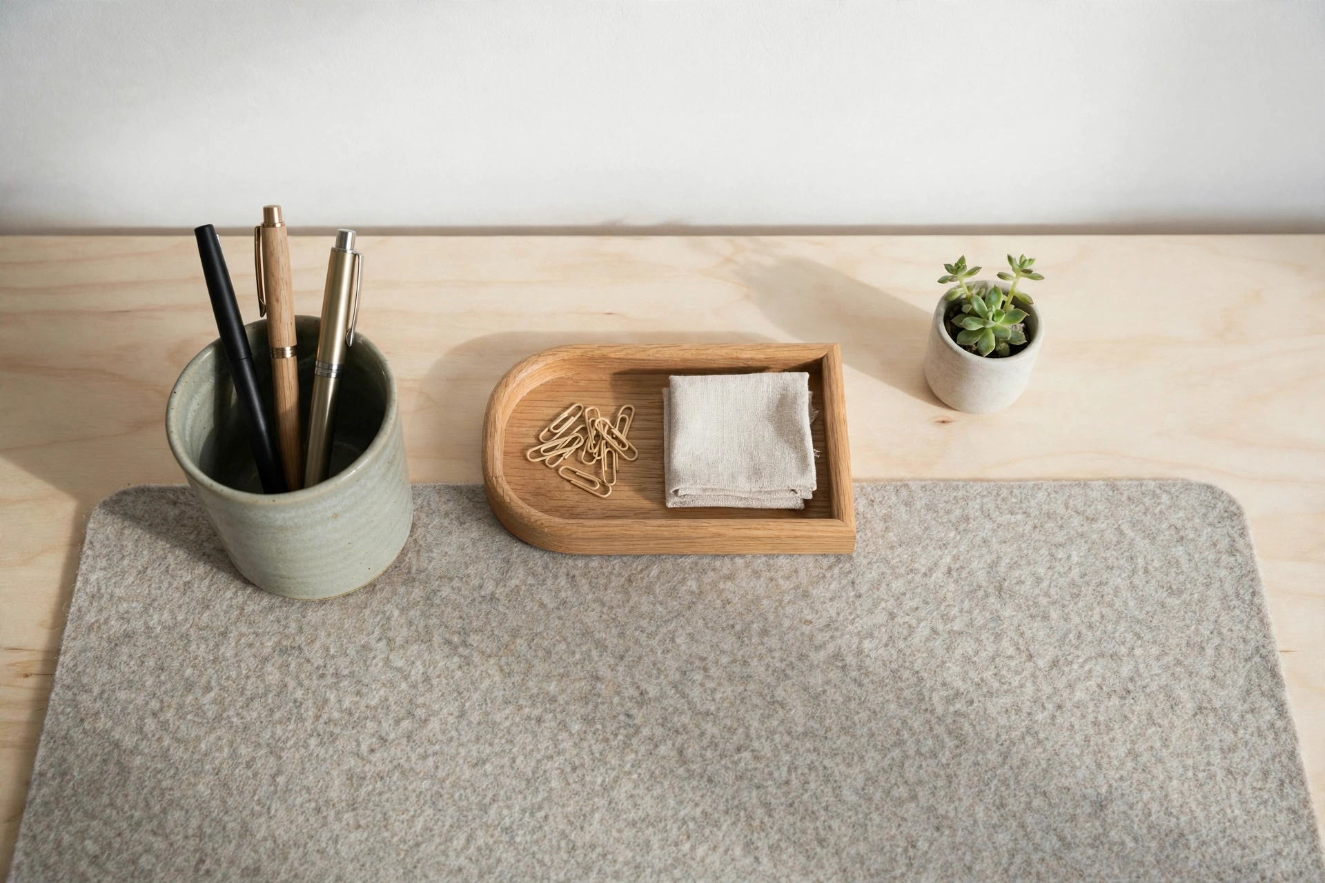 Stoneware pen cup, wool felt desk pad and oak tray on a pale wood Scandinavian desk